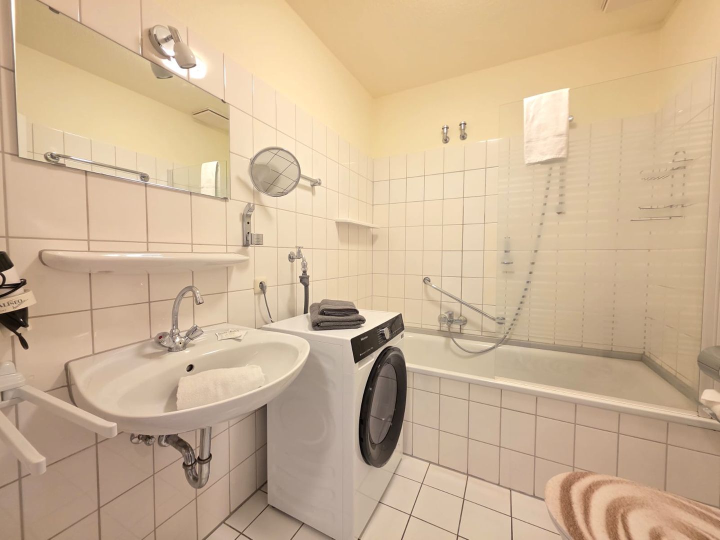 A bathroom with a sink, mirror, towel rack, and a washing machine.