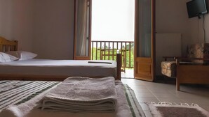 Ein Zimmer mit einem Bett, einem Fernseher, einem Balkon und einem Sessel.