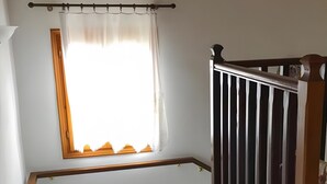 Eine Treppe mit hölzernem Geländer, ein Fenster mit Vorhang und ein Blumentopf.