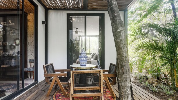 Eine Holzterrasse mit rundem Tisch und Stühlen, eine Glastür und Blick auf einen Garten.