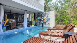 Ein Pool im Freien mit Holzliegen, ein Essbereich mit Stühlen und Tisch sowie eine Wand mit bunten Tellern.