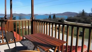 Een houten terras met een tafel en stoelen, met uitzicht op een meer en heuvels.