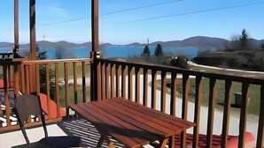 A wooden deck with a table and chairs, overlooking a lake and hills. - Studio Apartment 'Hotel Antigoni Triple Room 15' with Lake View, Wi-Fi and Air Conditioning (Neochori)