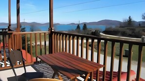 Eine Holzterrasse mit Tisch und Stühlen mit Blick auf einen See und Hügel.