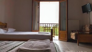 Ein Zimmer mit einem Bett, einem Fernseher, einem Balkon und einem Sessel.