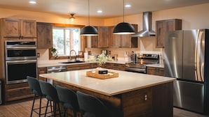 A modern kitchen with wooden cabinets, stainless steel appliances, and a central island with bar stools. - 28-Acre Olympic Cabin · Hot Tub + Sauna · Private (Port Angeles)