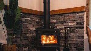 A cozy living room with a stone fireplace, a glass of wine, and comfortable seating. - 28-Acre Olympic Cabin · Hot Tub + Sauna · Private (Port Angeles)