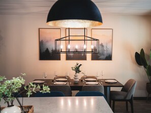 Un comedor con una mesa dispuesta para seis personas, una lámpara colgante moderna y tres cuadros de paisajes en la pared.