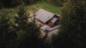 A cabin with a sloped roof, a deck, and a hot tub in a forested mountainous area. - 28-Acre Olympic Cabin · Hot Tub + Sauna · Private (Port Angeles)