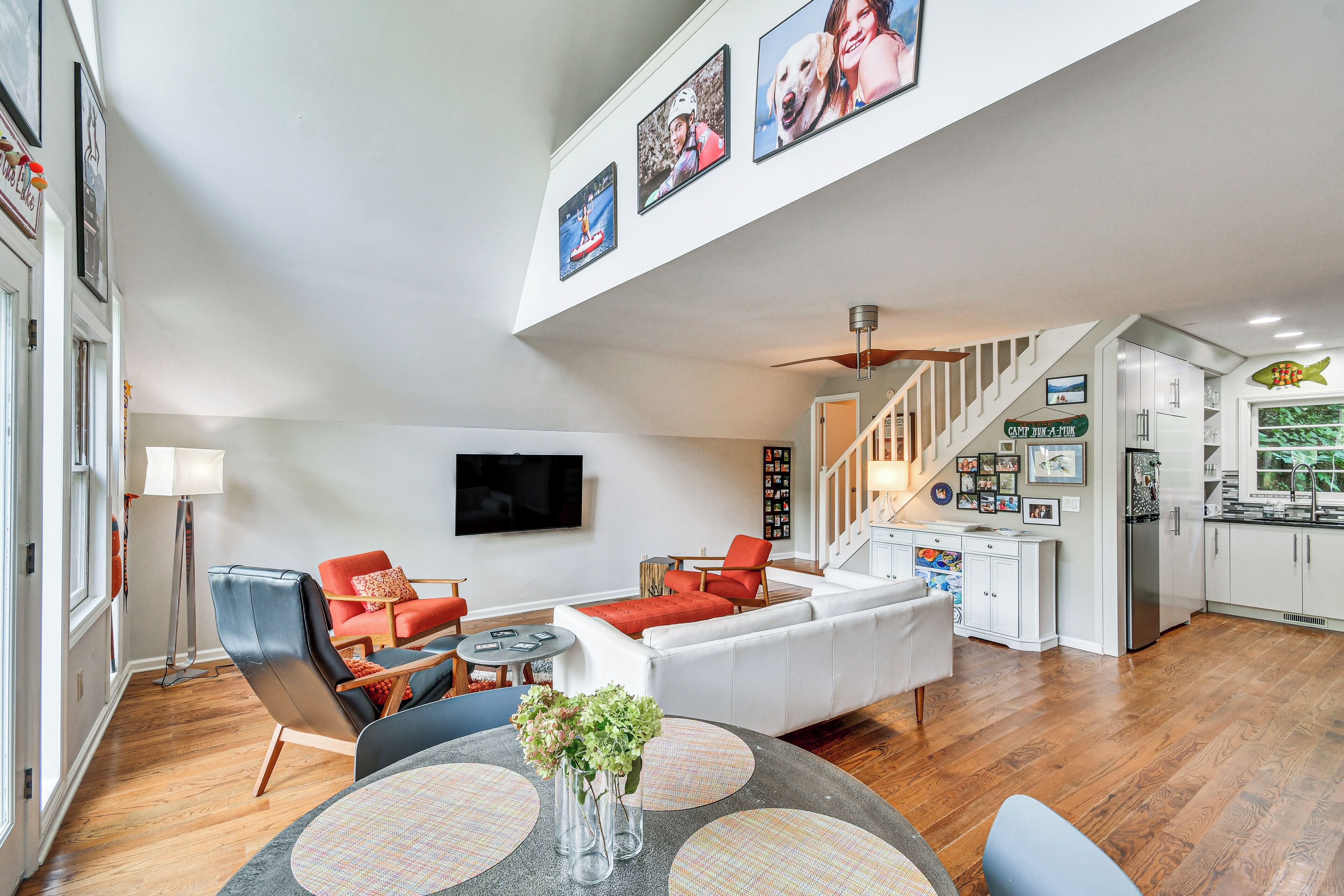 A spacious living room with a white sofa, red chairs, a dining table with placemats, and a staircase leading to a kitchen area.