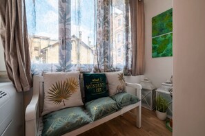 Eine gemütliche Sitzecke mit einer Bank, einem Fenster mit Vorhängen und einer Wand mit einem Gemälde von grünen Blättern.