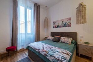 Ein Schlafzimmer mit Bett, Vorhängen, einer Pendelleuchte, einem Wandbild und einem Nachttisch.
