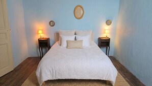 Een slaapkamer met een bed, twee nachtkastjes met lampen, een spiegel aan de muur en een deur.