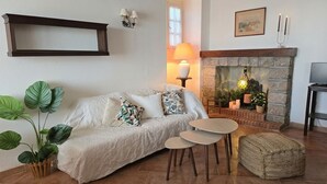 Een gezellige woonkamer met een bank, twee ronde tafels, een open haard en een plant.