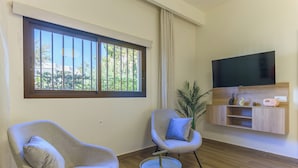 Una sala de estar moderna con dos sillones, un televisor, una mesita, una planta en maceta y un mueble bajo para el televisor.