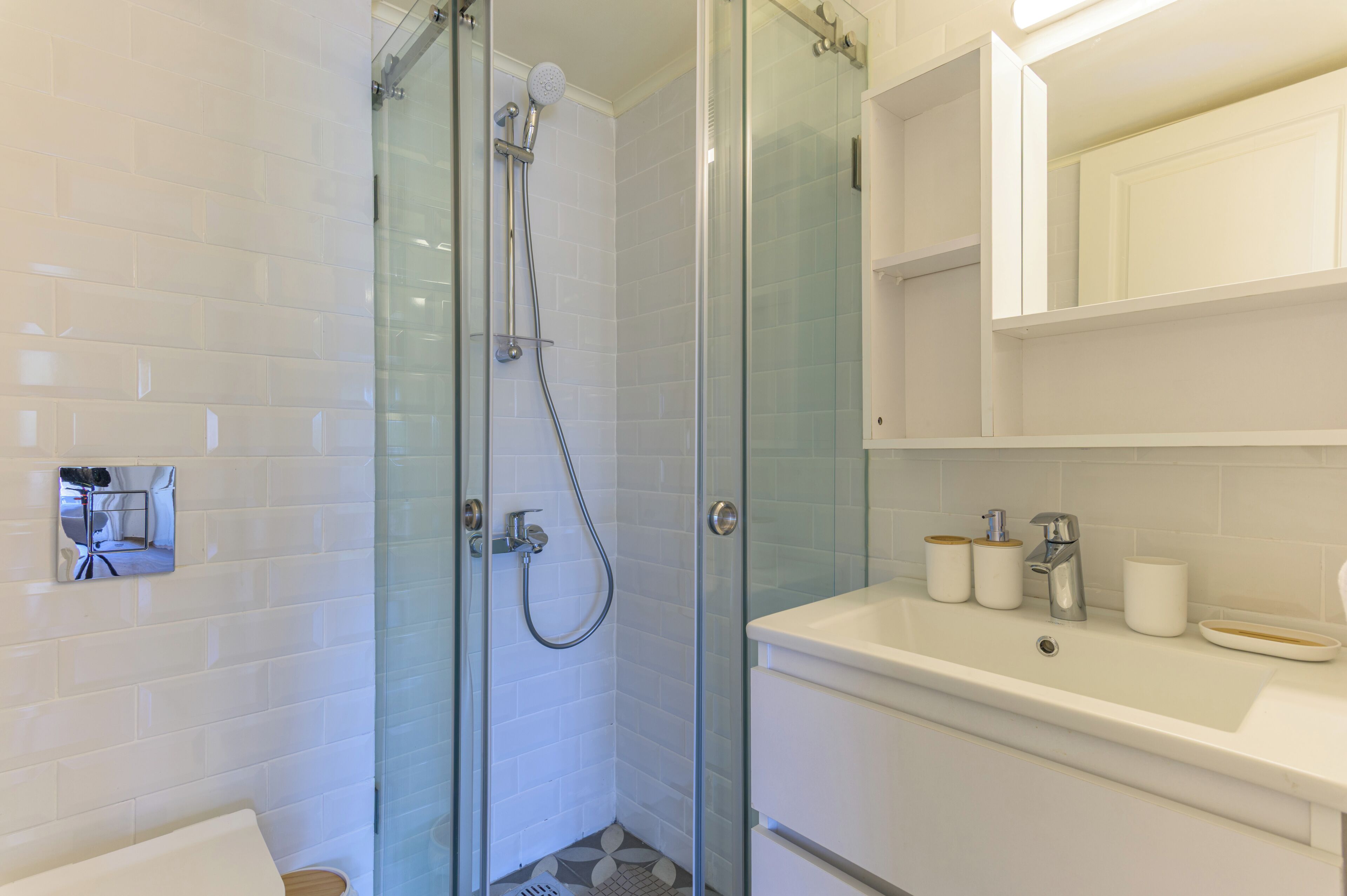A modern bathroom with a glass-enclosed shower, white tiled walls, a white sink, and a mirror cabinet.