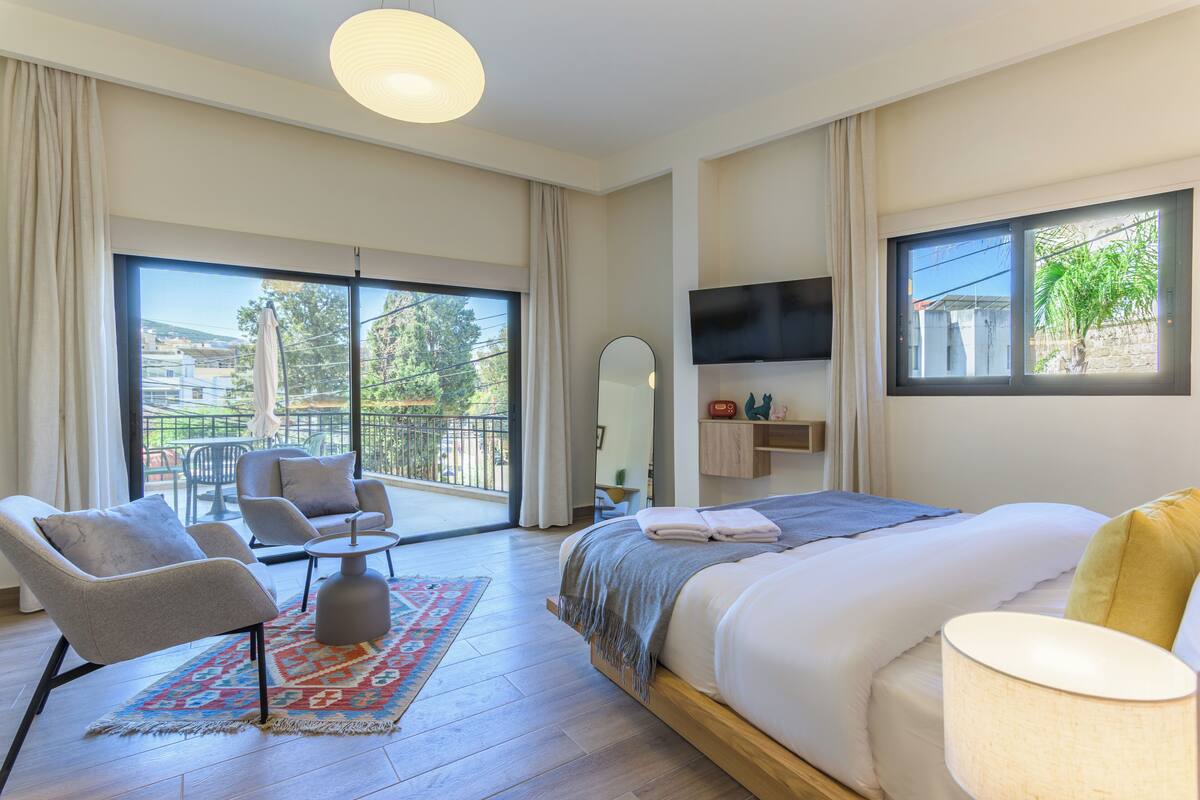 Une chambre dotée d’un grand lit, d’une télévision, d’un balcon avec vue et d’un coin salon avec des fauteuils.