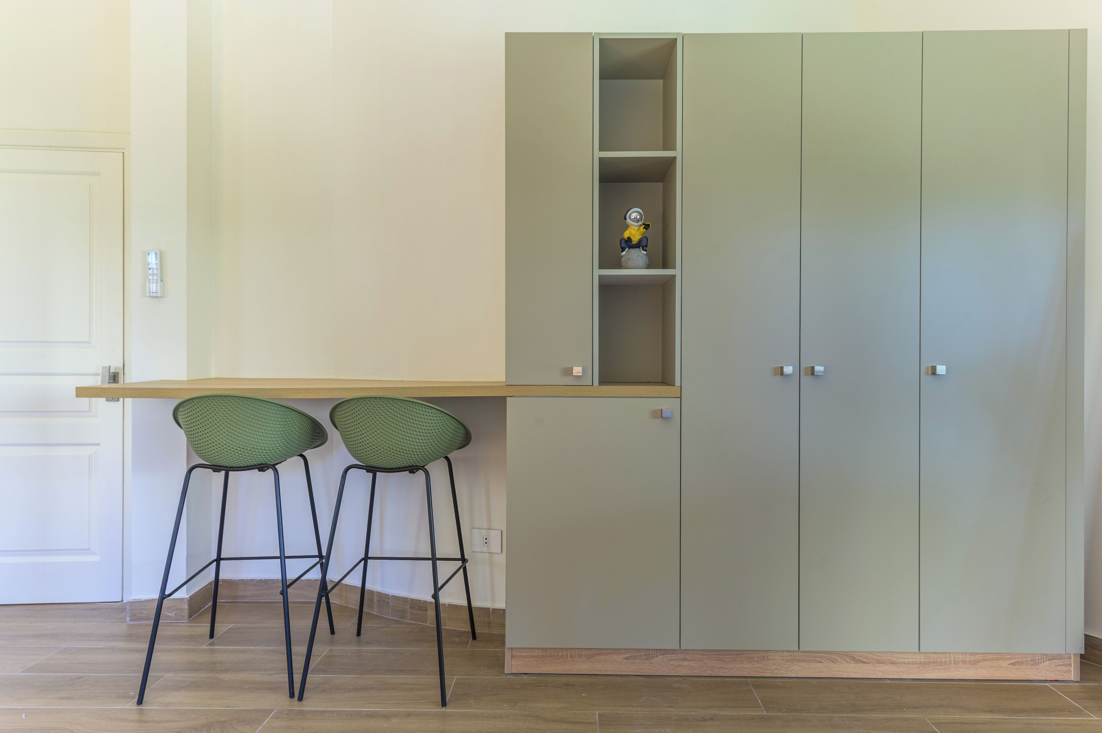 A kitchenette with a built-in cabinet, two green chairs, and a small shelf with a figurine.
