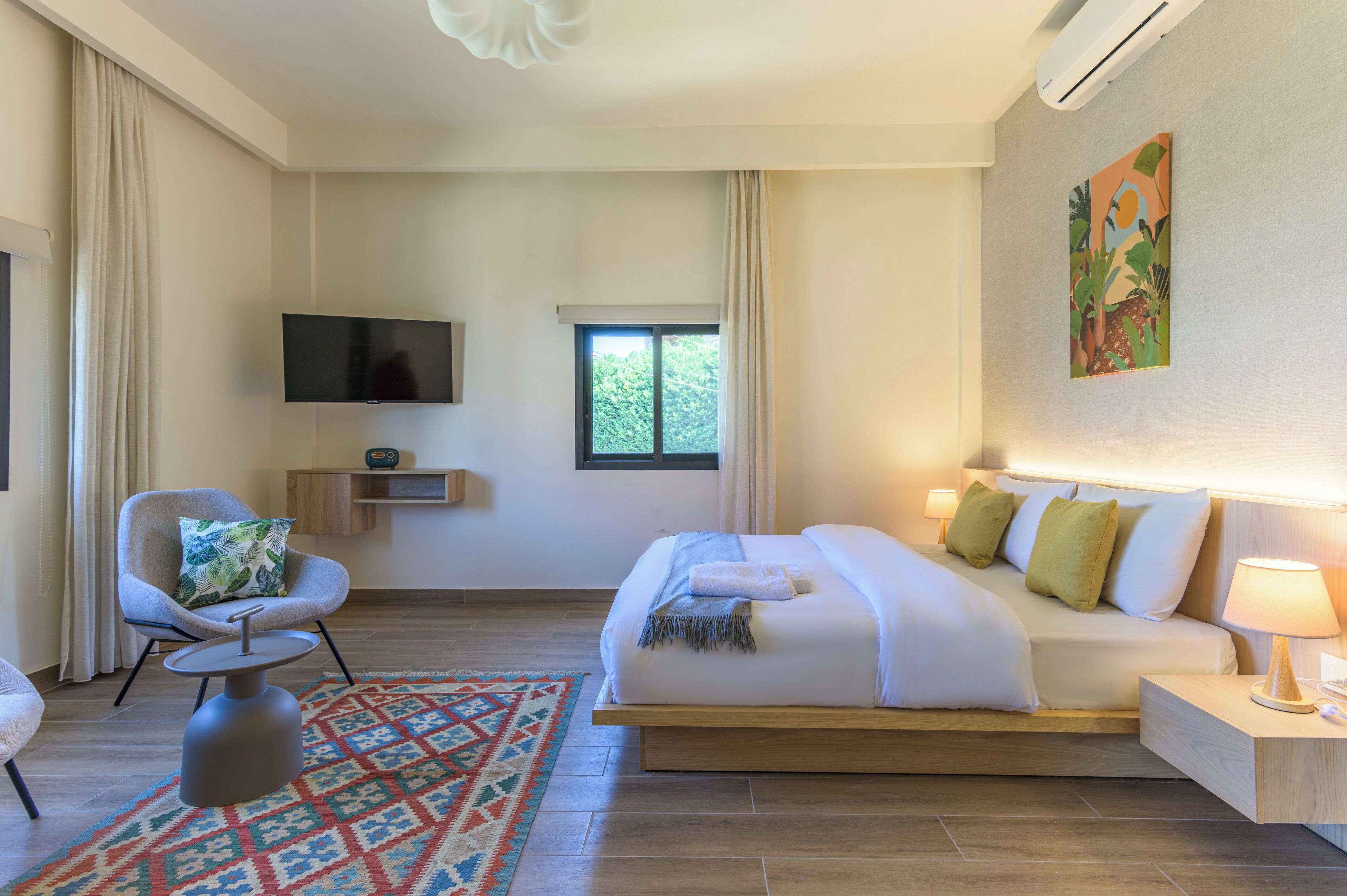 A modern hotel room with a bed, bedside table, chair, TV, and a window with curtains.