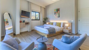 Una habitación de hotel moderna con una cama grande, un televisor, una mesita de noche con lámpara, una silla y una pequeña mesa.