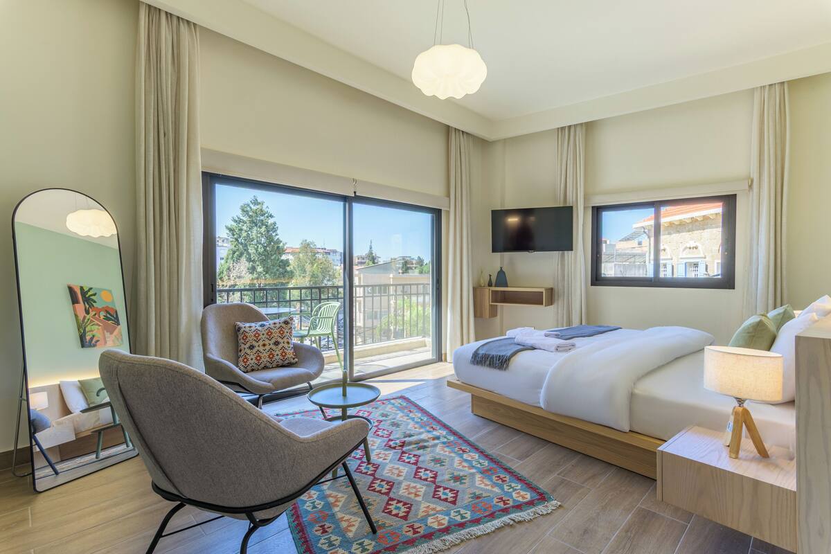 Une chambre d’hôtel avec un lit, une chaise, une télévision, un balcon et une grande fenêtre.