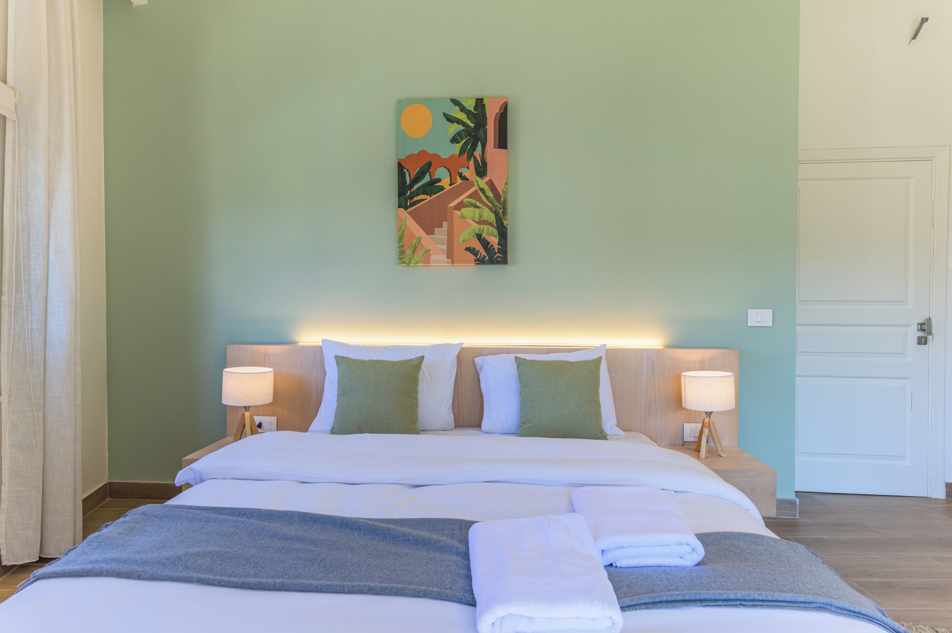A hotel room with a bed, two bedside lamps, a painting on the wall, and a door.
