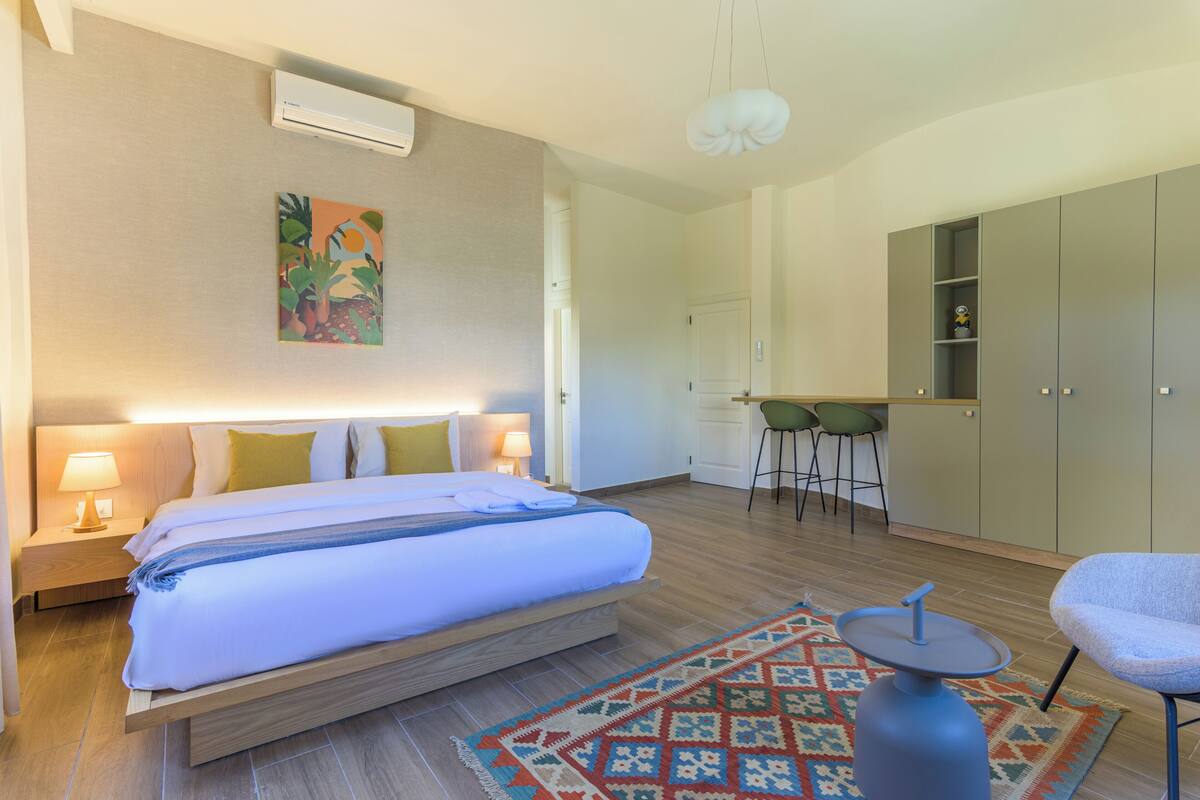 Une chambre d’hôtel comprenant un lit, des lampes de chevet, un petit bureau, une chaise, une kitchenette et une armoire.