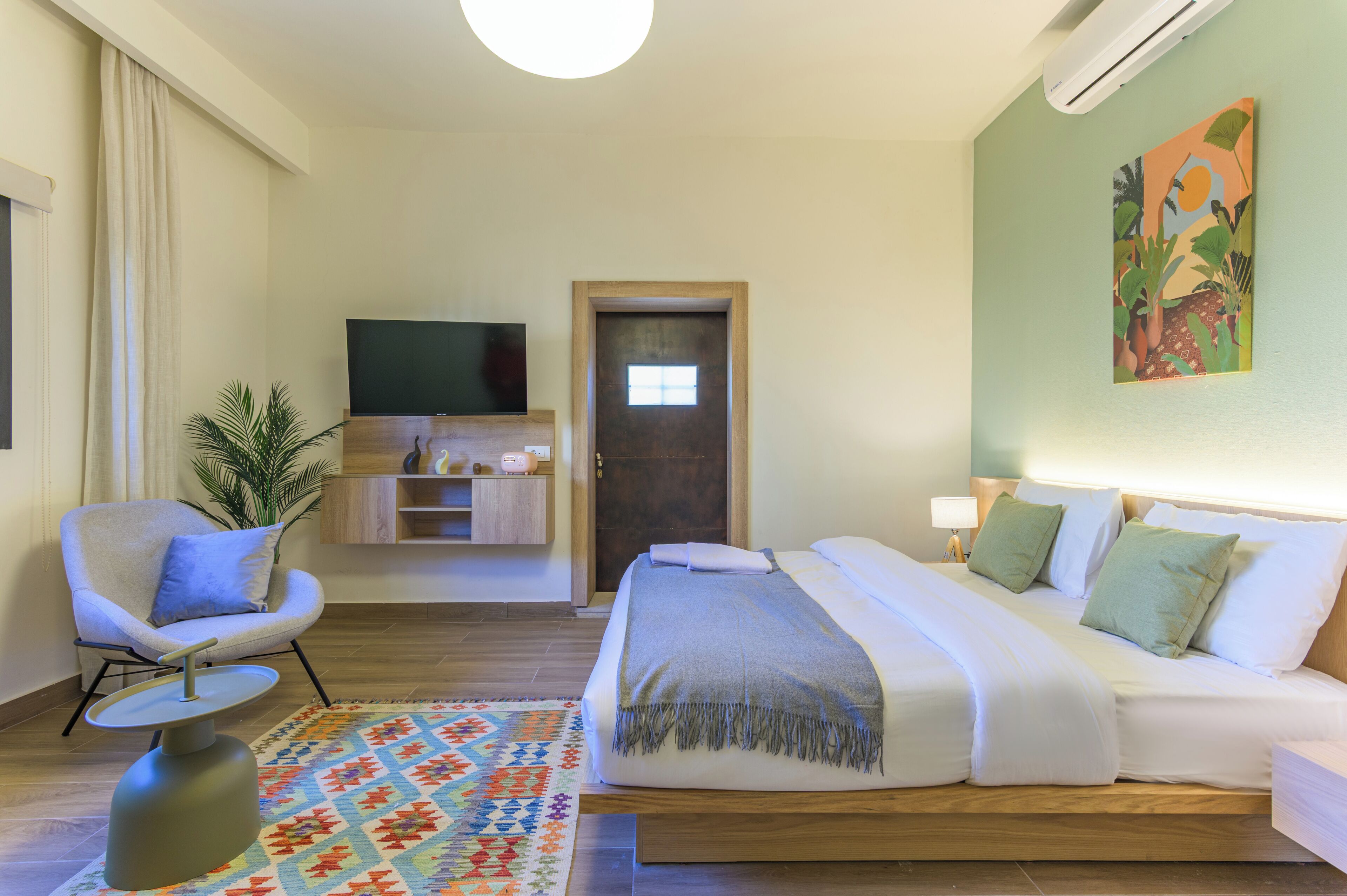 Une chambre d’hôtel avec un lit, une chaise, une télévision, une petite table et un tableau au mur.
