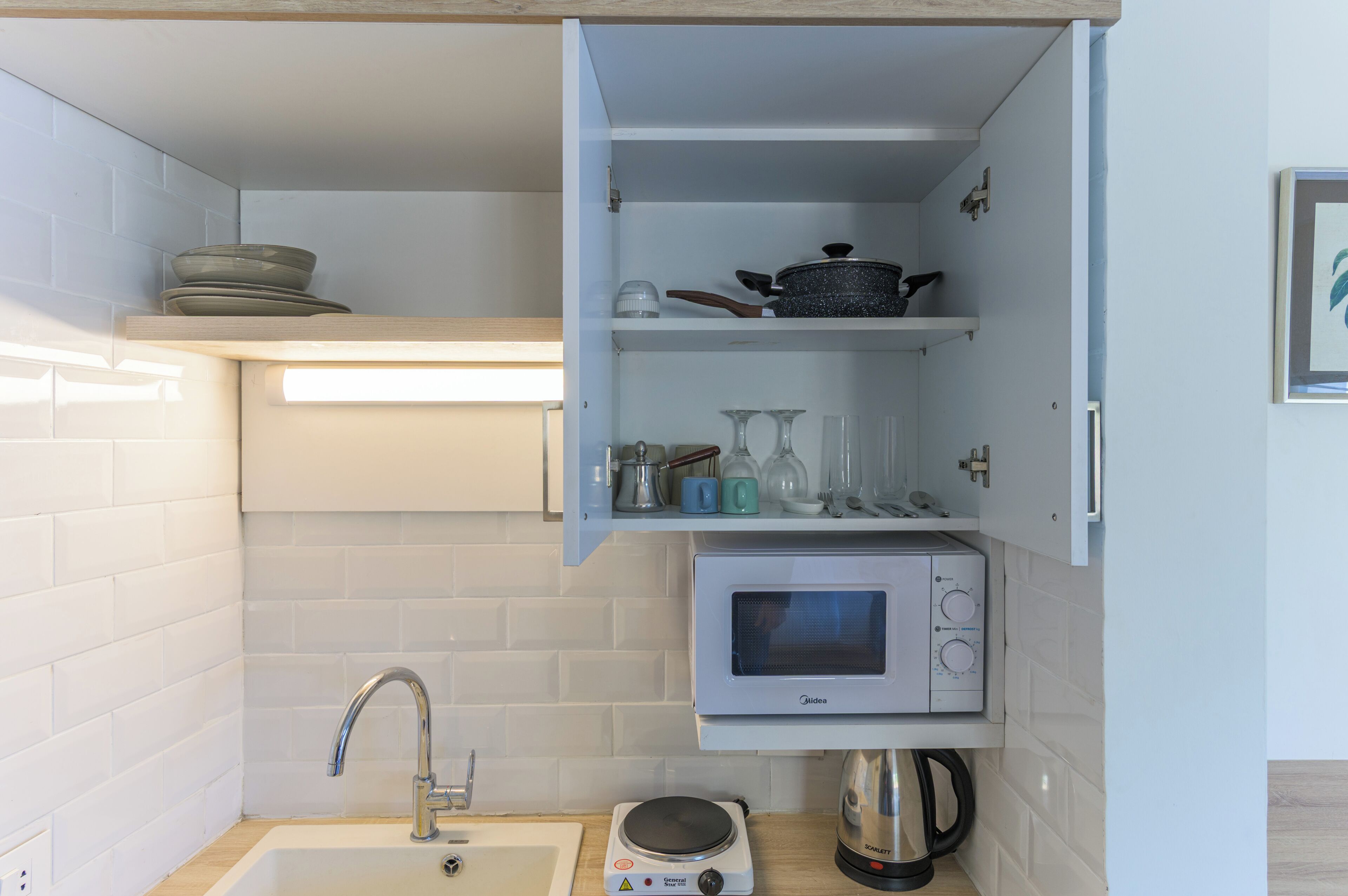 Una cocina compacta con microondas, hervidor y pileta.