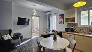 A compact living space with a dining table, a sofa, a TV mounted on the wall, a kitchen area with a microwave, and a window with a view. - Zante Cozy Apartment (Zakinthos)