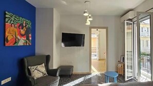 A living room with a blue wall, a grey sofa, a small round table, and a TV mounted on the wall. - Zante Cozy Apartment (Zakinthos)