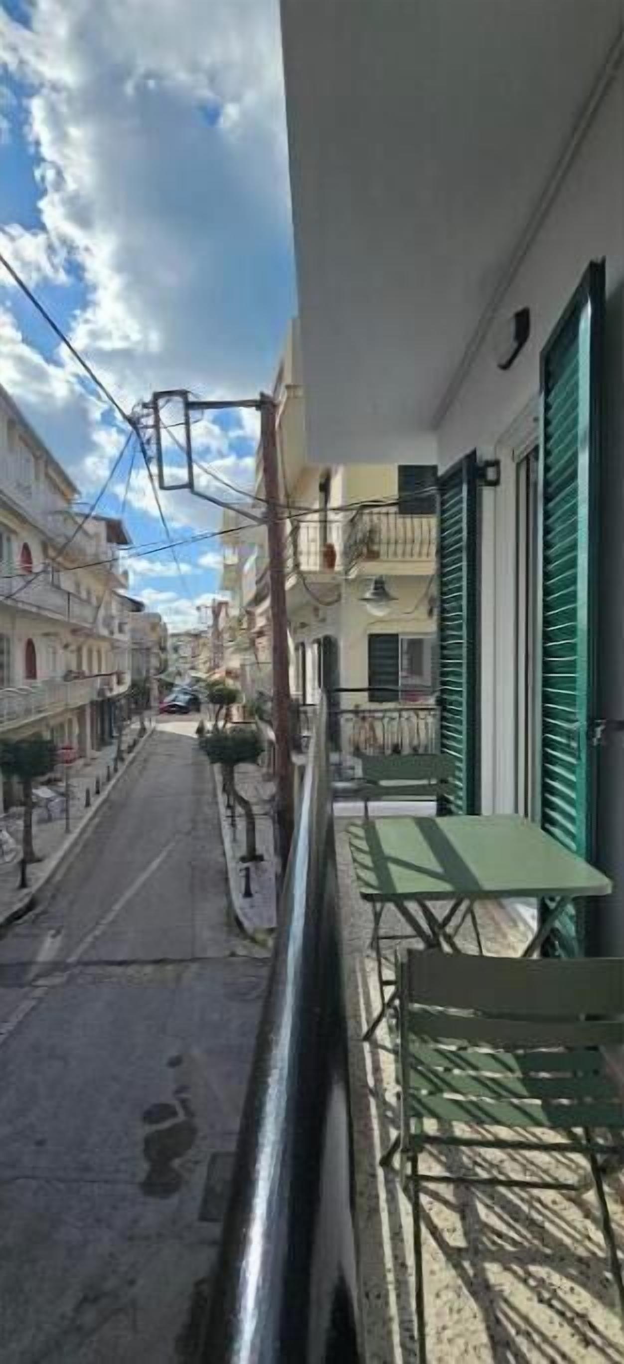 Een smalle straat met gebouwen aan beide zijden, een balkon met tafel en stoelen, en bovengelegen elektriciteitskabels.