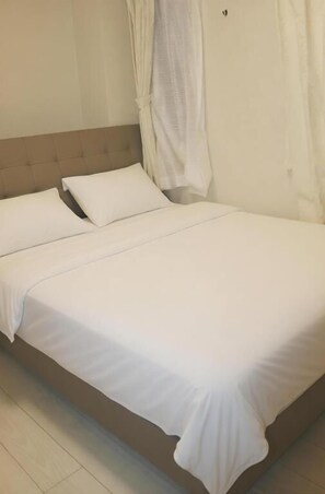 Ein Einzelbett mit weißer Bettwäsche, einem Kopfteil und einem Vorhang.