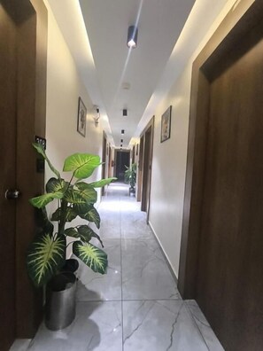 A hallway with a potted plant, a trash can, and a door with a number sign. - Hotel Royal Villa  (Ahmedabad)
