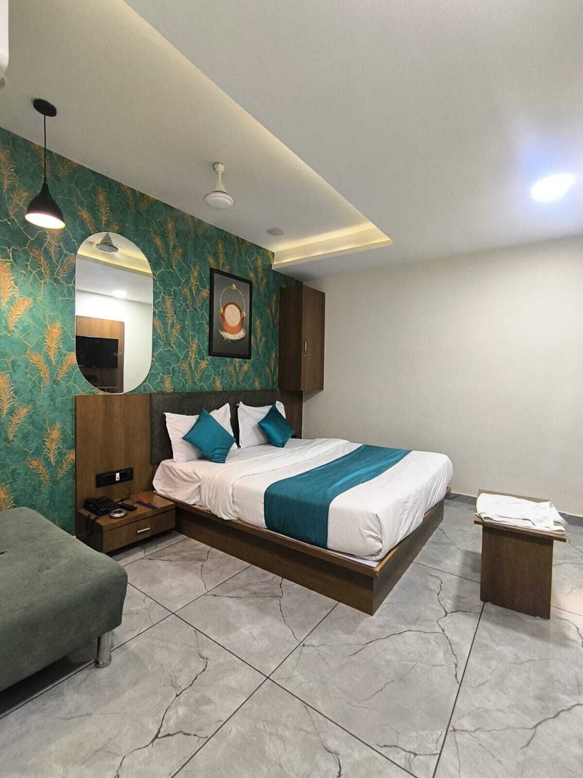 A modern hotel room with a bed, bedside table, lamp, and a small table with a chair.