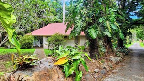 Ein kleines Haus mit rotem Dach, umgeben von üppigem Grün und einem gepflasterten Weg.
