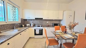 Une cuisine moderne avec des meubles blancs, des plans de travail en granit, une cuisinière et un coin repas avec des chaises orange.
