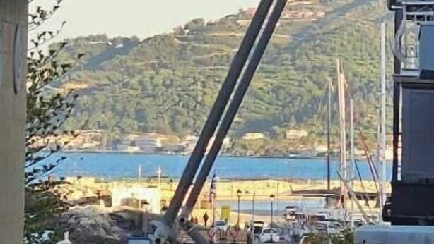 Une vue d’une zone côtière avec un pont, des voitures garées et quelques personnes qui se promènent.