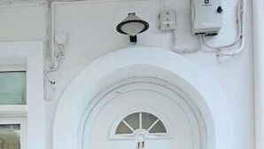 Une porte blanche surmontée d’une arche en demi-cercle, une petite fenêtre à carreaux et un bouton de sonnette au-dessus de la porte.