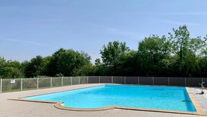 A rectangular swimming pool with a tiled deck, surrounded by a metal fence and trees in the background. - Nature Cottage Near Puy du Fou (Moutiers-Sous-Chantemerle)