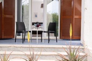 A modern outdoor seating area with two chairs and a table, a staircase leading to an upper level, and a view of a building with a balcony. - Villa Comar (Forio)