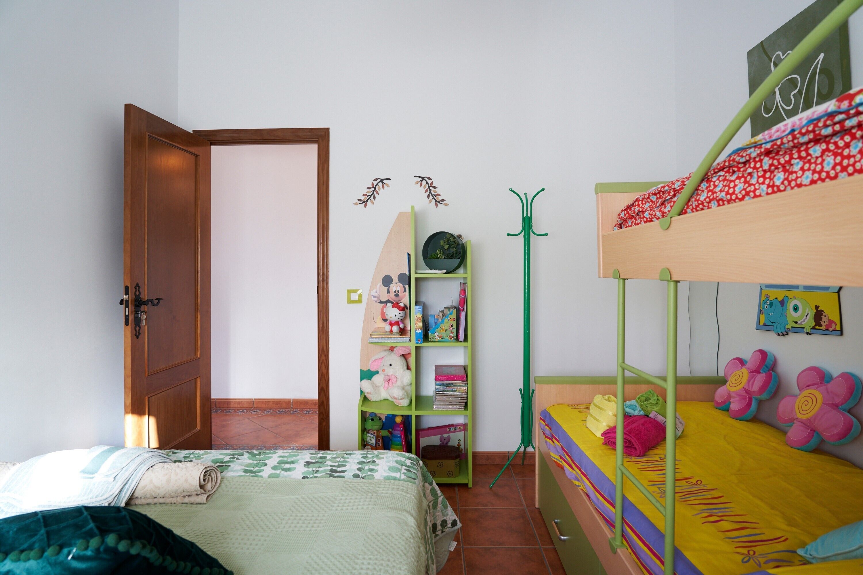 Camera da letto per bambini con letti a castello, una libreria verde e una porta che dà su un'altra stanza.