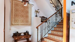 A staircase with patterned tiles, a wooden console table with decorative items, and a hanging tapestry.