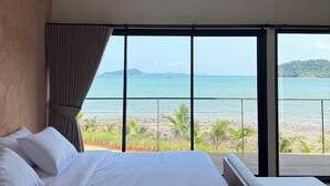 Une chambre avec un grand lit, un ventilateur de plafond et une vue sur la plage et l’océan.