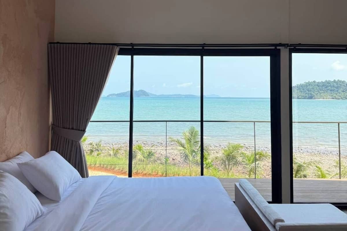 A bedroom with a large bed, a ceiling fan, and a view of the beach and ocean.