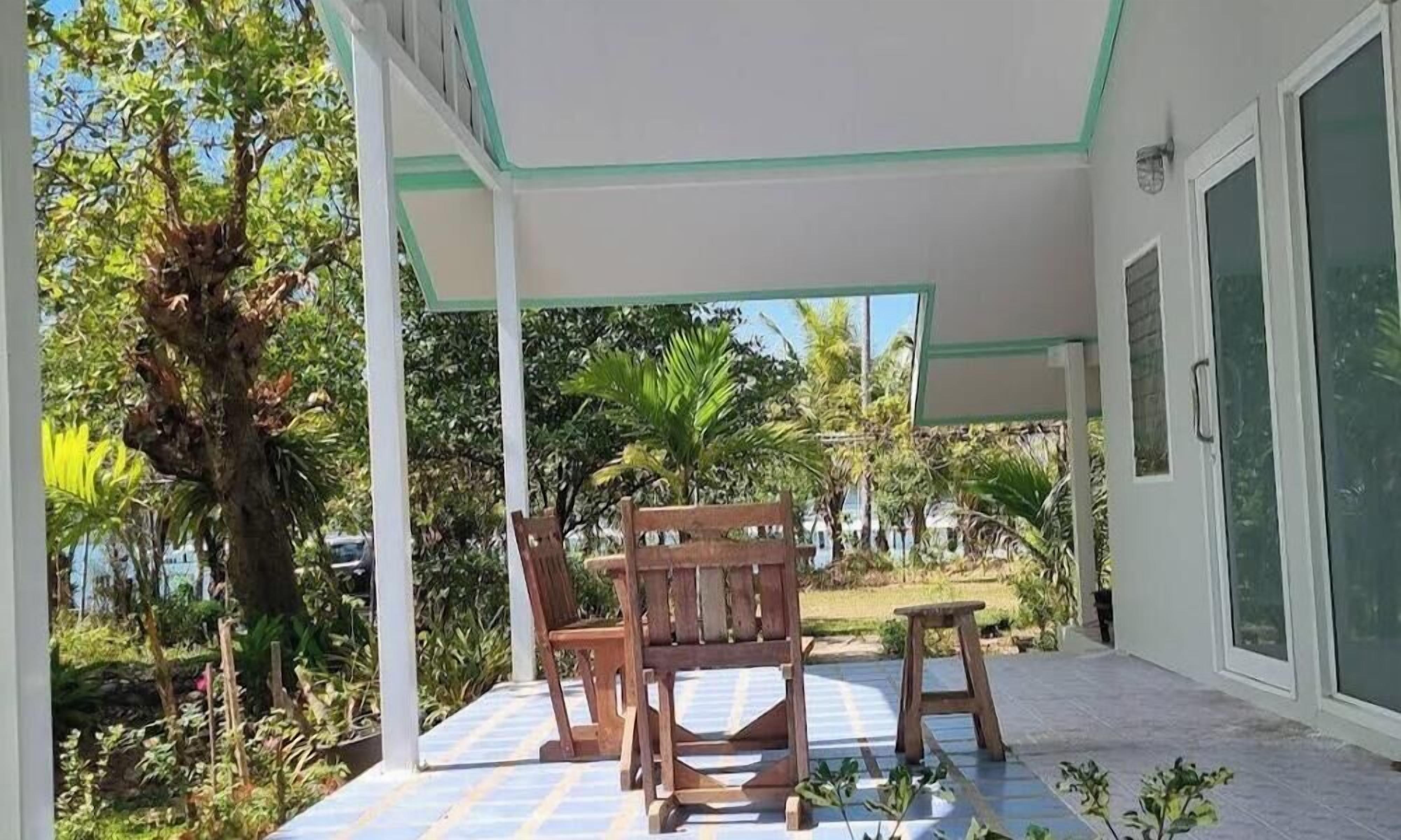 Un espacio al aire libre cubierto con sillas de madera y una mesa, rodeado de abundante vegetación y un cielo despejado.