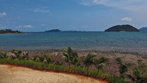 Une plage bordée d’un rivage rocheux, avec des palmiers et des îles qui se dessinent à l’horizon.