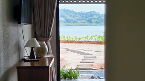 Une chambre d’hôtel avec un bureau en bois, une lampe, un téléviseur fixé au mur et une vue sur un lac et des montagnes, visible à travers une grande fenêtre.