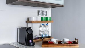 Una cafetera, botellas de agua, tazas y una bandeja con galletas sobre una encimera.