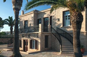 Ein zweistöckiges Gebäude mit einer Stein-Fassade, einem Balkon mit schwarzen schmiedeeisernen Geländern und einer Treppe, die zu der oberen Etage führt.